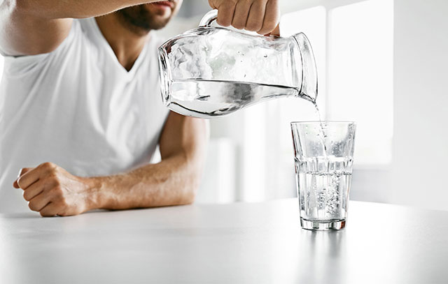 Wasser aus Krug wird in Glas eingeschenkt